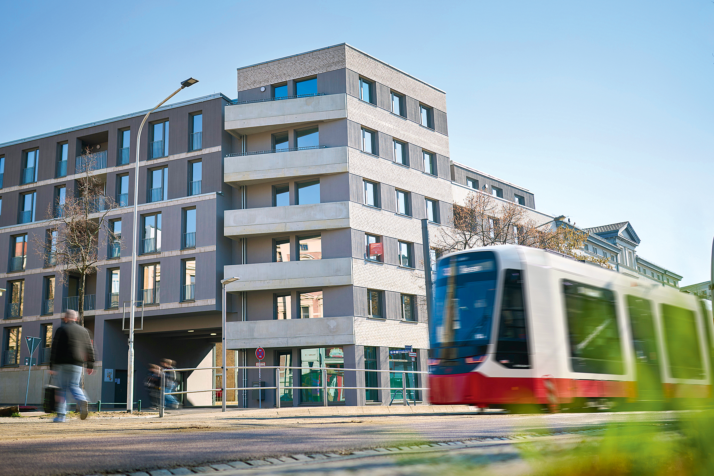 Gebäudeansicht mit fahrender Straßenbahn davor.
