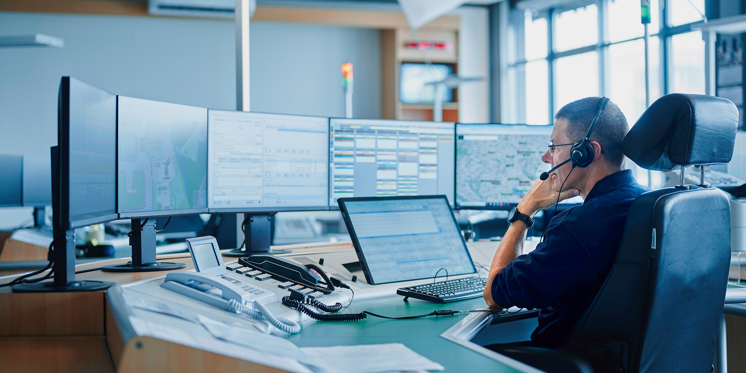 Mann sitzt vor vielen Monitoren in einer Leitstelle.