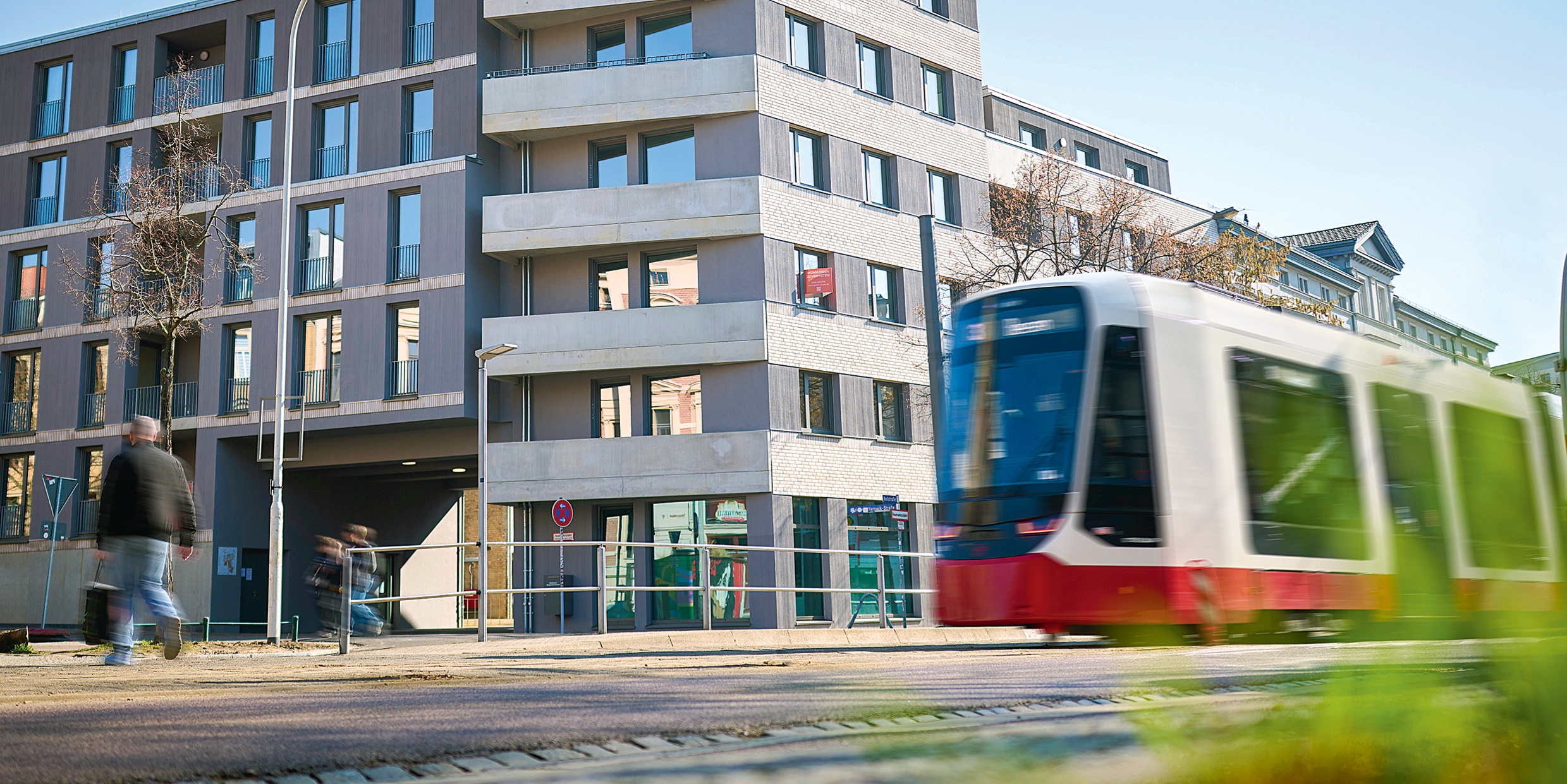 Gebäudeansicht mit einer fahrenden Straßenbahn davor.